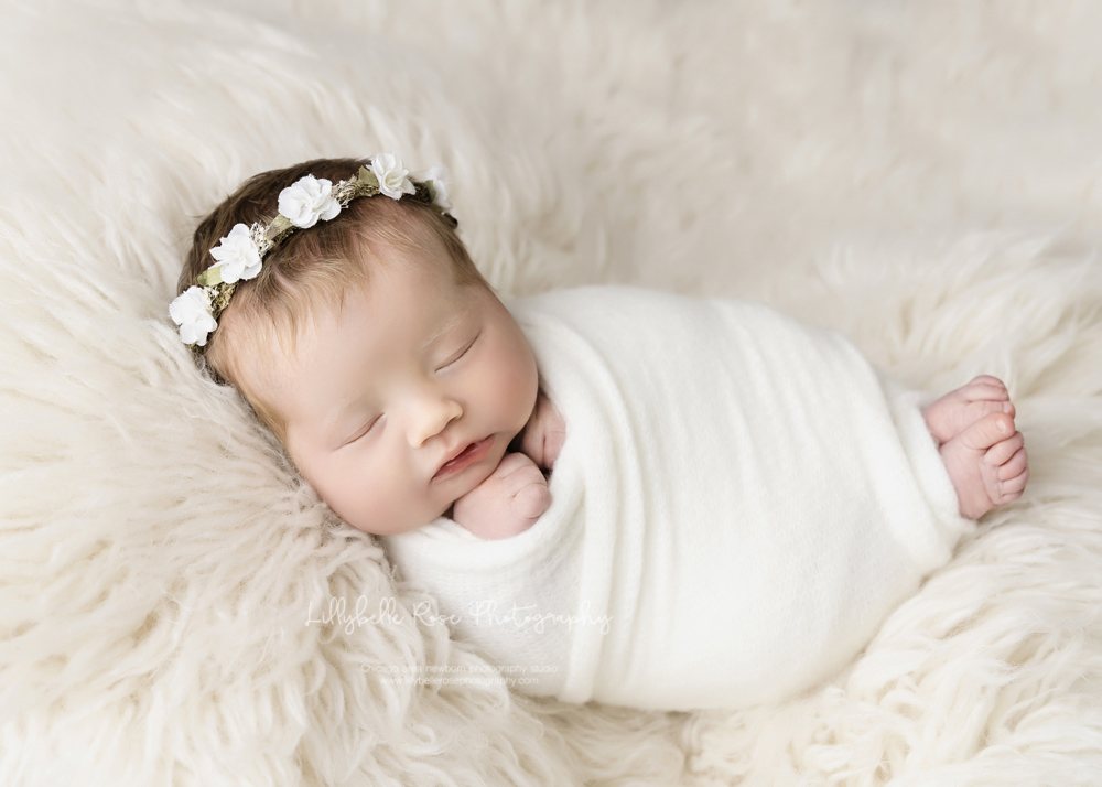 swaddled newborn on cream fur with floral crown