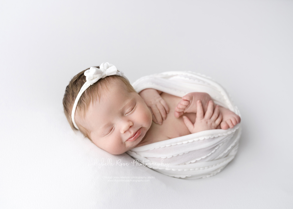 smiling newborn on white in wrap with toes and fingers details