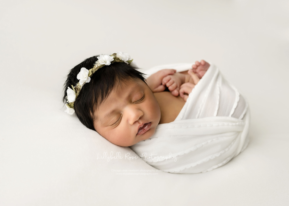 newborn in white swaddle with floral crown