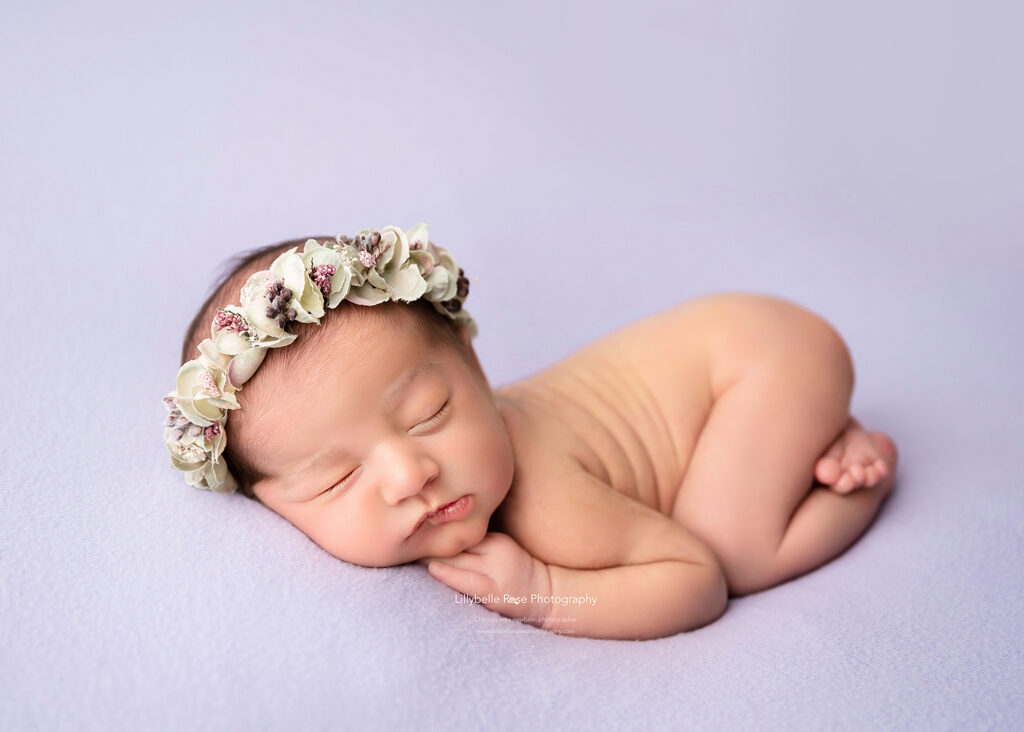 newborn in cute pose on purple fabric with a floral wreath headband