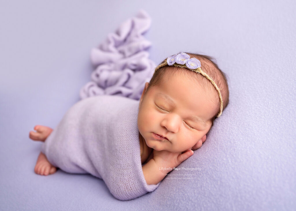 adorable newborn baby posed on purple fabric with purple wrap and floral headband