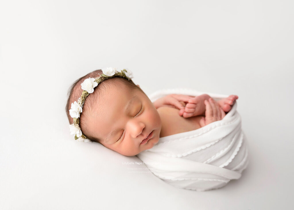 grinning newborn baby girl on white with swaddle and headband