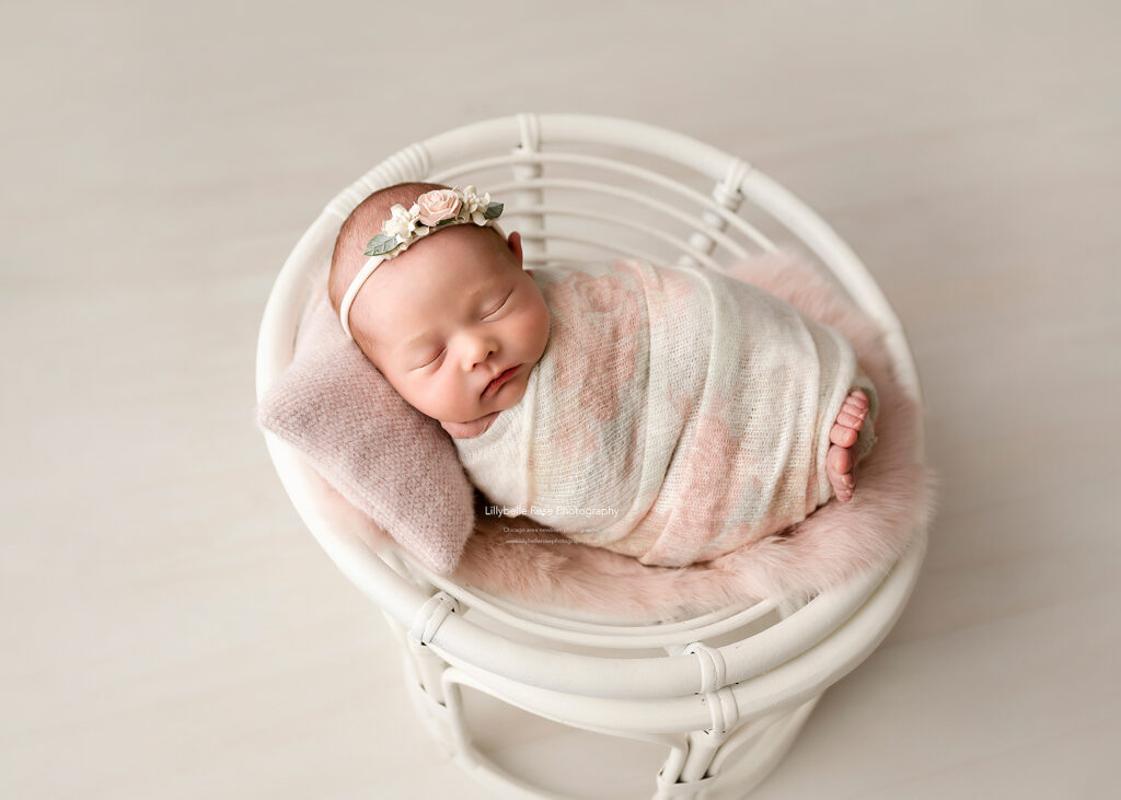 sleeping baby on papason chair wrapped in floral wrap with pink pillow and headband
