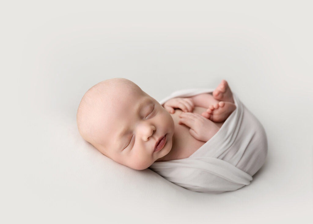 newborn wrapped in white with fingers and toes showing