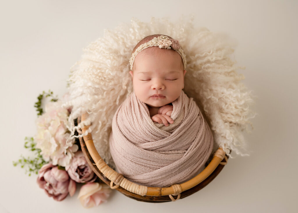 timeless newborn portraits, sleeping baby in pink swaddle posed in a basket with pink and mauve flowers 