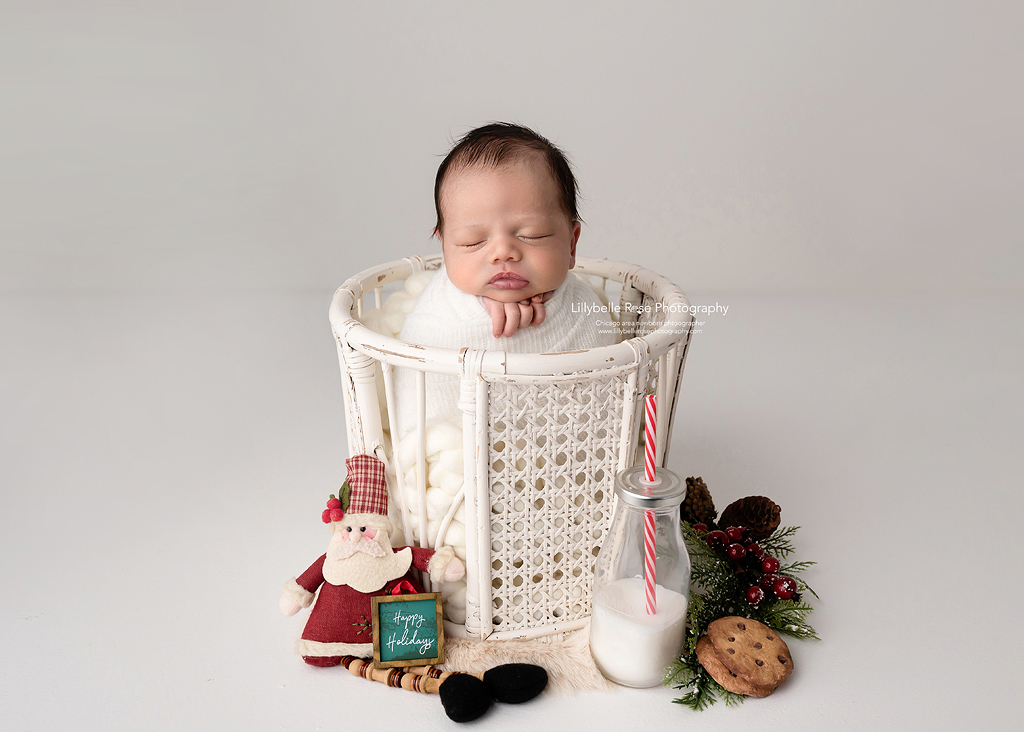 Baby in a white basket with Christmas accessories and milk and cookies for Santa