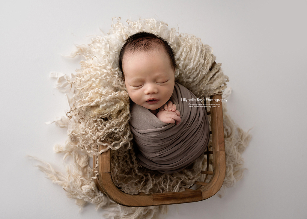 Sleeping baby in basket with tan fur and a brown wrap.