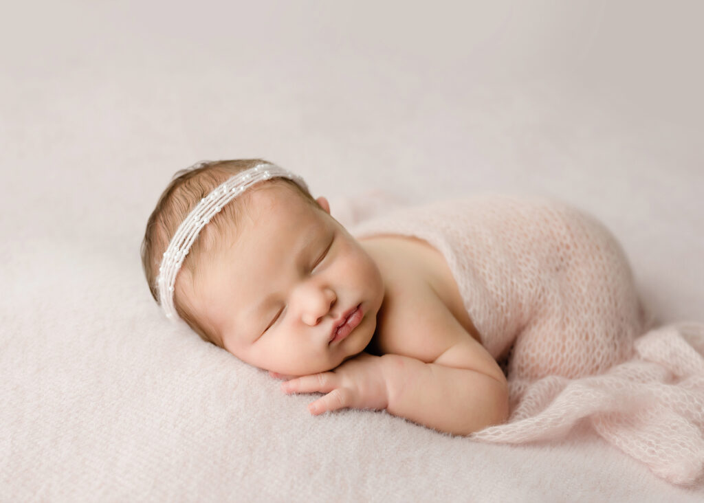 Sleeping baby girl on a pink backdrop with a pink wrap and pearl headband