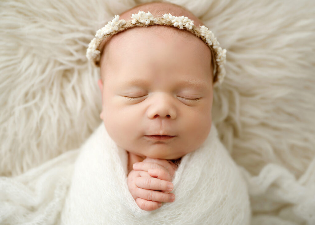 Baby girl grinning in her sleep while holding her hands under her chin.