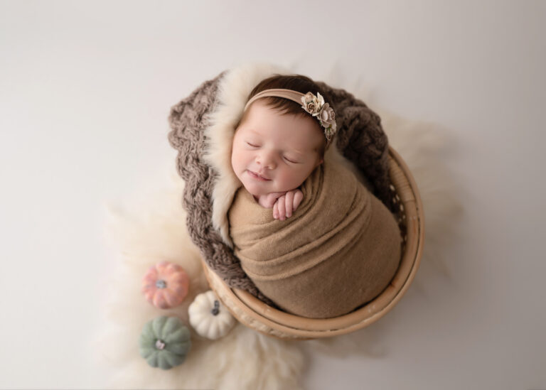 Newborn Photographer, a baby girl sleeps in a small basket looking very happy with a smile