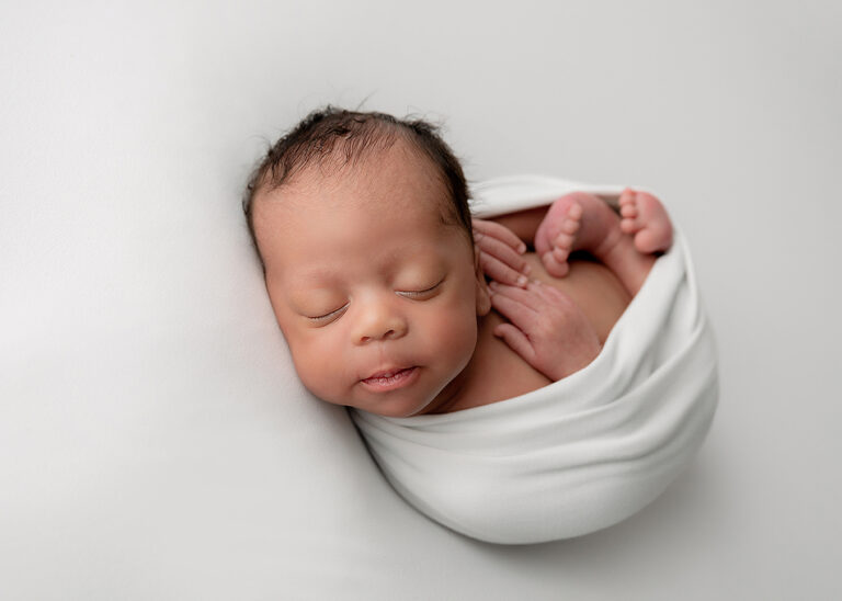 Newborn Photographer, a little baby sleeps snuggles into a little white blanket.