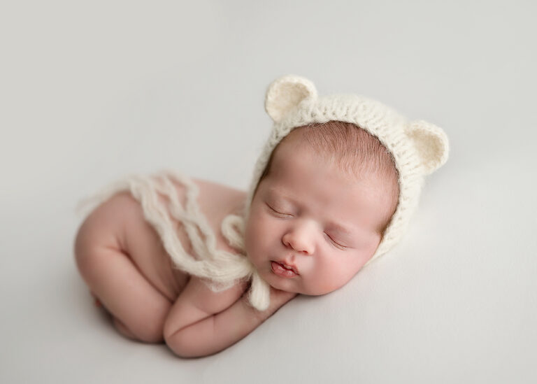 Newborn Photographer, a baby sleeps with an animal bonnet around her head.
