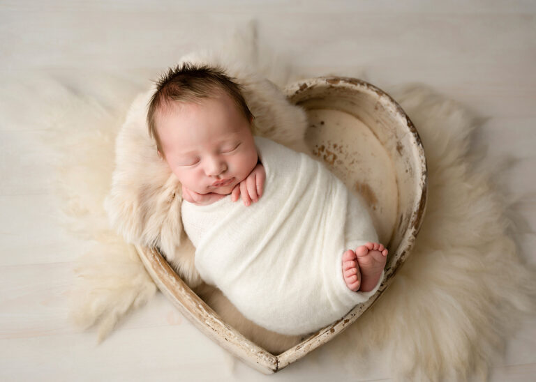 Newborn Photographer, a baby girl sleeps in a small heart shaped basket peacefully.