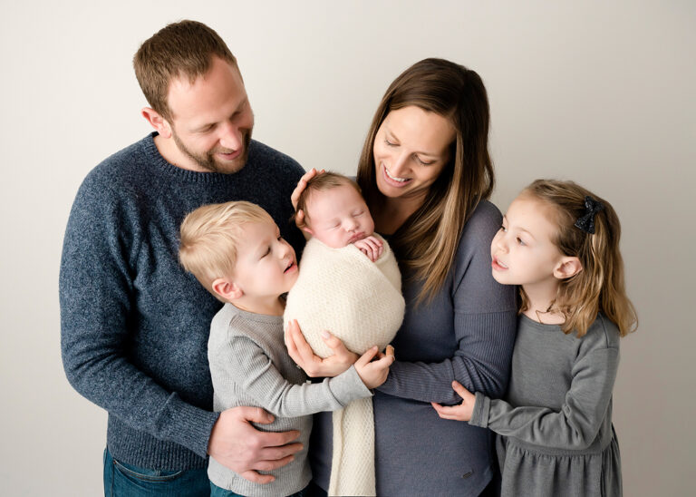 Newborn Photographer, a mother holds her new baby as dad and two older siblings look on.
