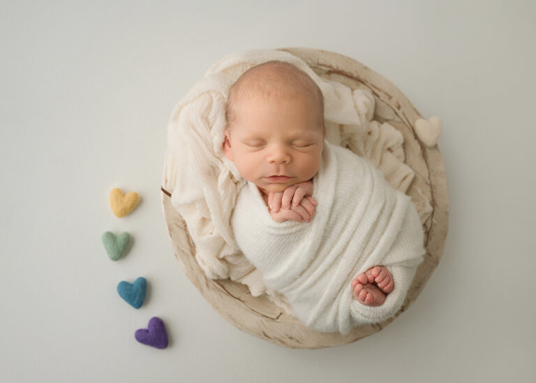 Newborn Photographer, a little baby sleeps in a small basket with littler woven heart near her.