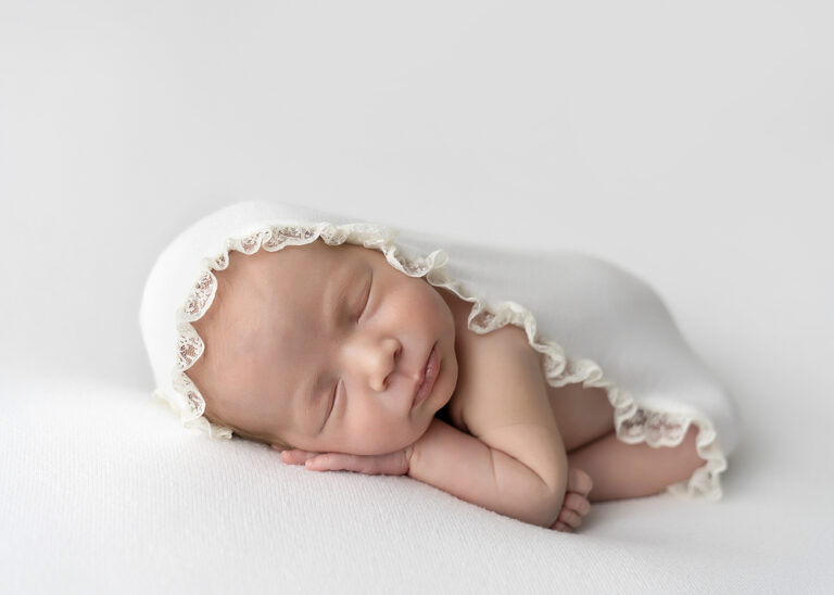 Newborn Photographer, a baby girl sleeps beneath a frilly white blanket.