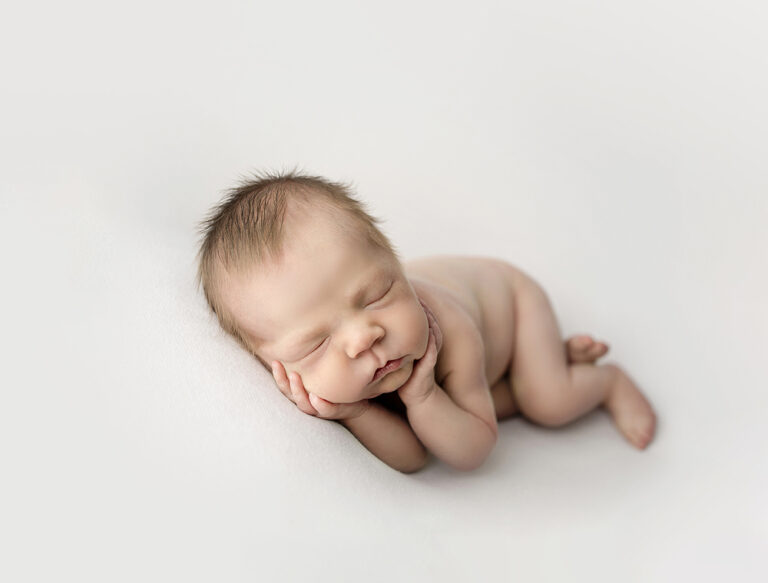 Newborn Photographer, a little baby sleeps with his arms tucked beneath him.