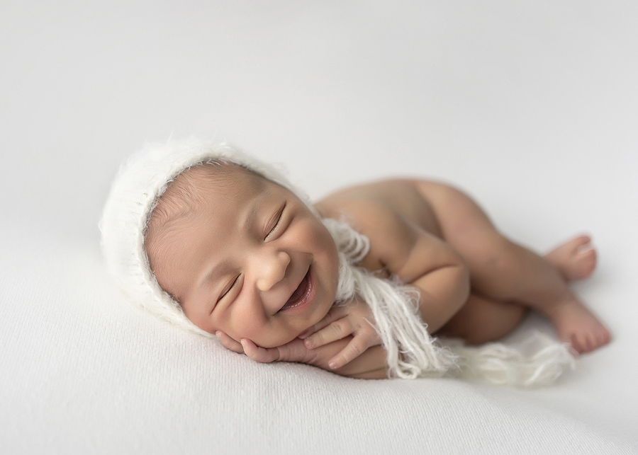 Newborn Photographer, a baby smiles while sleeping with a knit bonnet on her head